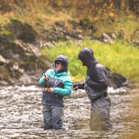 Two anglers share a laugh while wading knee deep in the river.