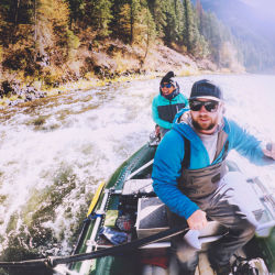 Two excited anglers in a raft riding over some rapids.
