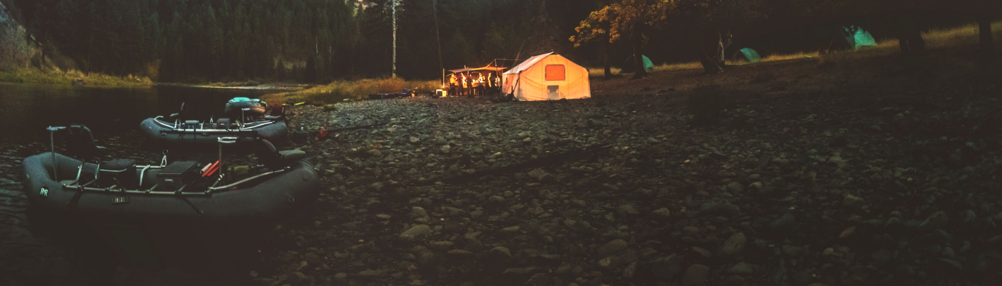 Evening on a riverbank with a lit up tent