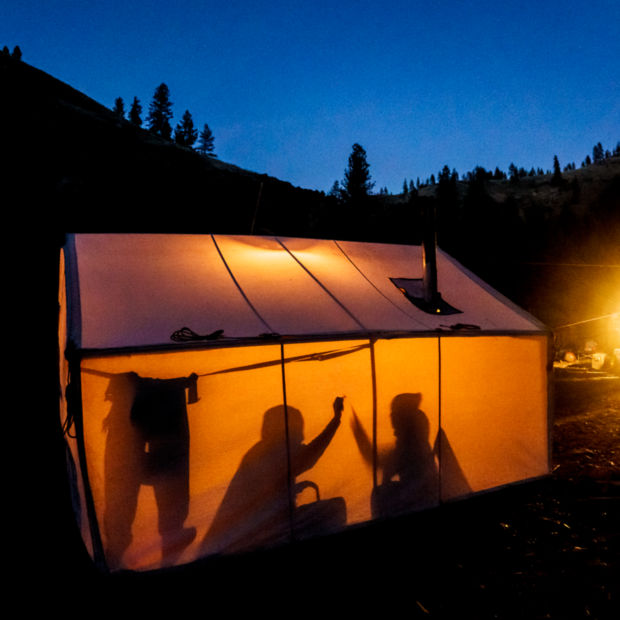 Two peoples silhouettes darken the bright sides of a wall tent.