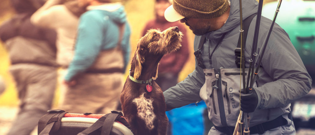 An angler wearing PRO Zip waders gives his dog some attention