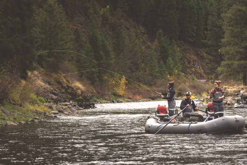 Two anglers casting from a raft on a river while a third angler rows.