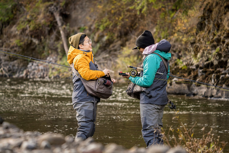Two anglers stand face to face in the river.