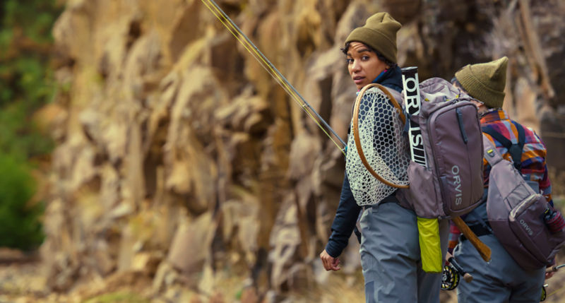 A woman looking over her shoulder wearing a backpack that houses her rod