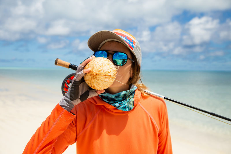 A woman by the beach wearing a ball cap and sunglasses.