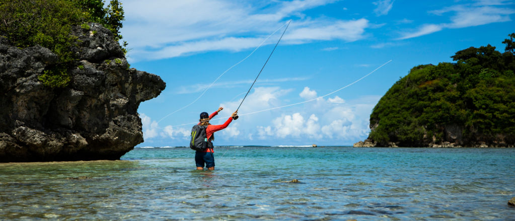 An angler casts her fly line from thigh-deep in tropical waters.