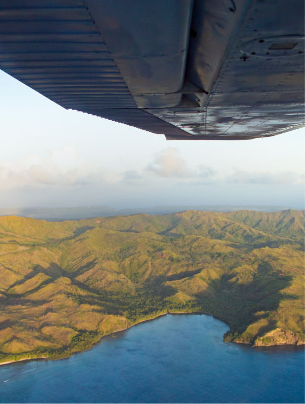 Aerial view from a plane, showing the plane's wing and the mountainous landscape below.