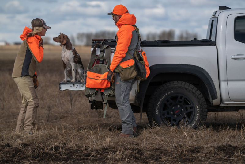 A hunter gears up with her dog and guide behind a pickup truck.