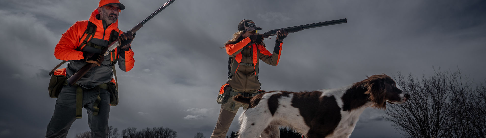 Two hunters aim their shotguns under a cloudy sky