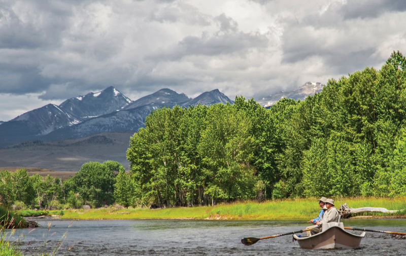 Two men in a drift boat with mountains in the background.