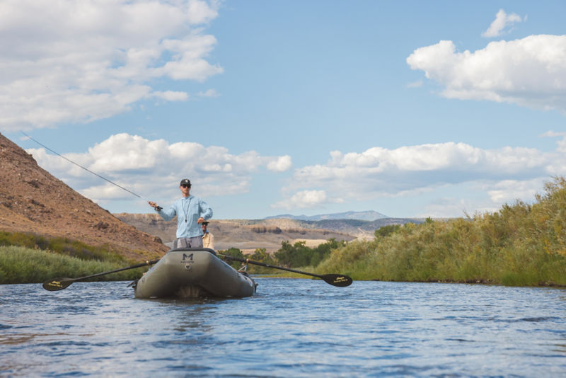 An angler stands in a raft casting his Helios Fly Rod.