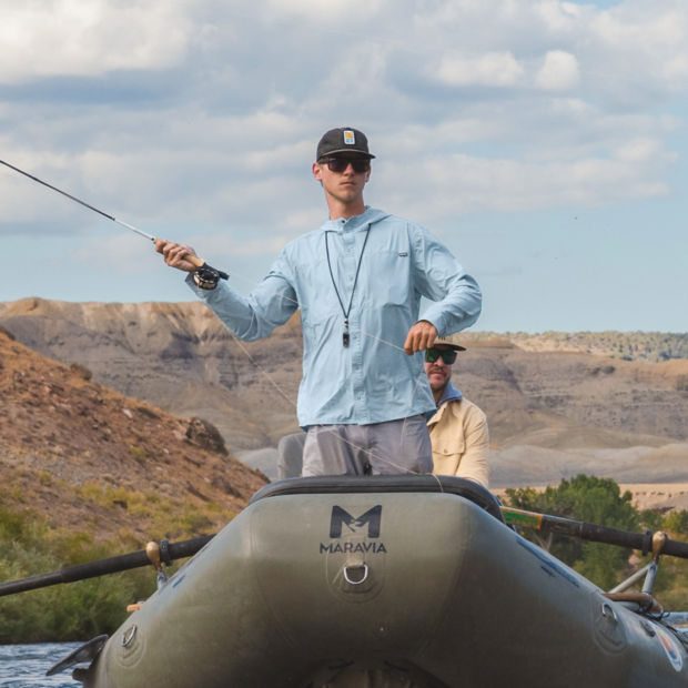 An angler stands in a raft casting his Helios Fly Rod.