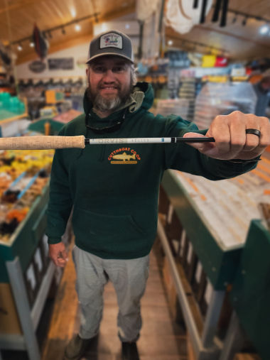 A smiling man holds up a new Helios Rod in a shop.