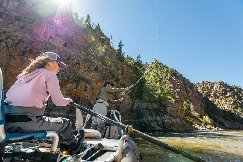 Two anglers in a raft heading down river.