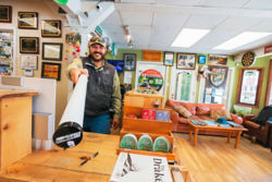 A man holding a Helios Fly Rod standing inside a fly shop.