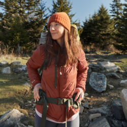 A woman wearing a salmon-colored mid-weight jacket and winter hat while hiking outside