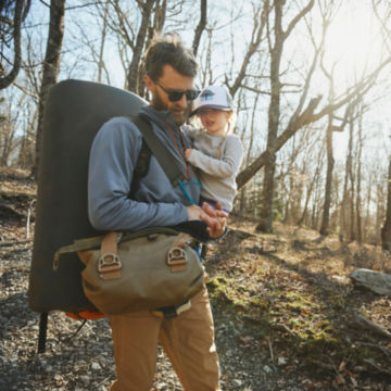 A man in a Bluestone Horseshoe Hills Quarter-Zip Fleece takes his daughter through the woods with camping gear.