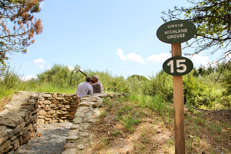 A student and an instructor behind a stone wall practicing their shot.