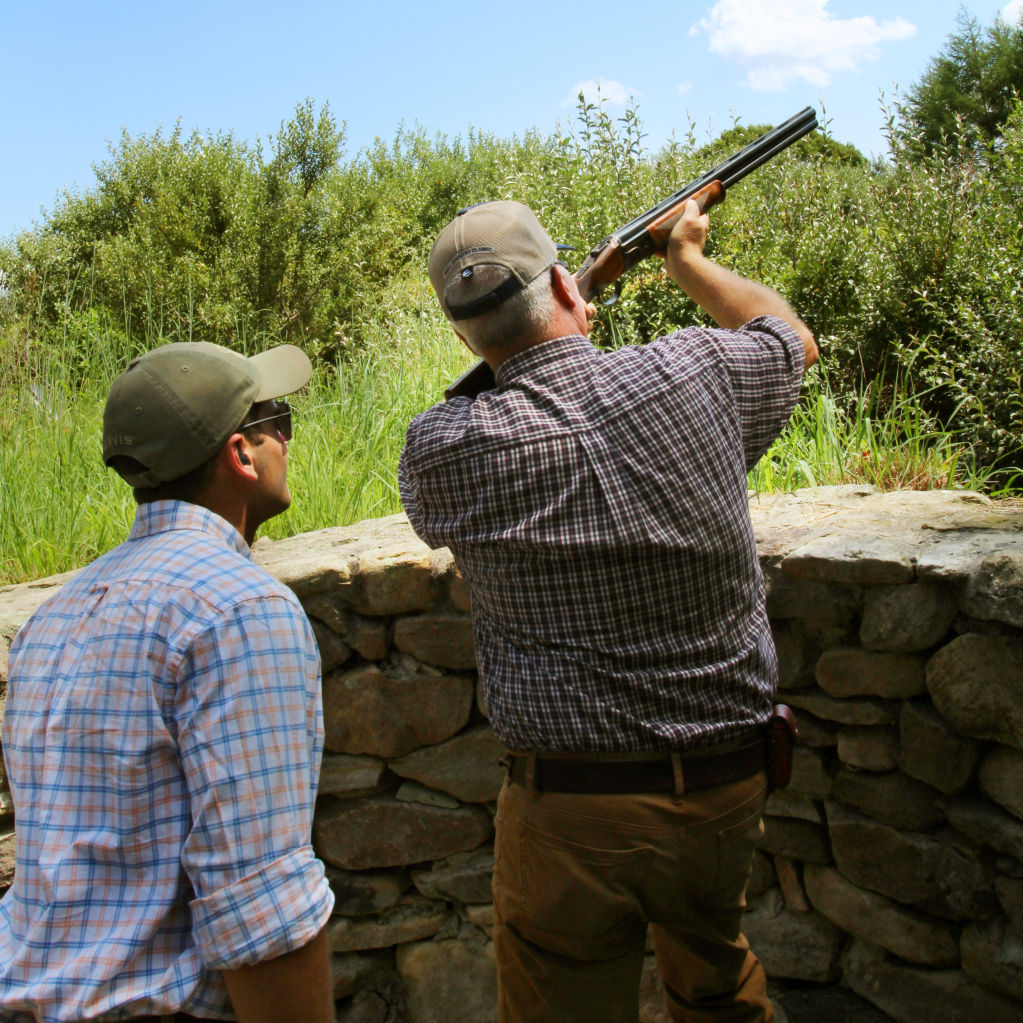 Two men behind a stone wall practicing their shot