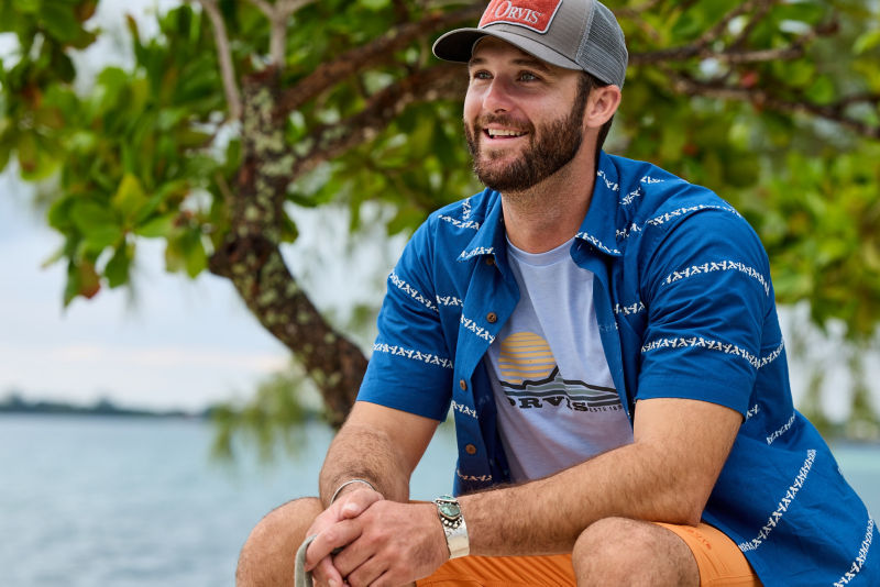 A man sitting outdoors wearing a t-shirt and a button-down.