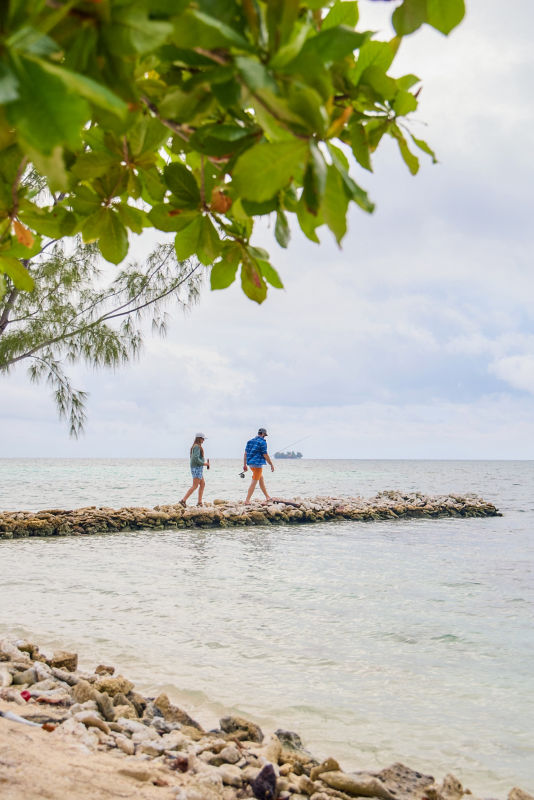 A couple walking out onto a stone outcrop into a tropical sea.