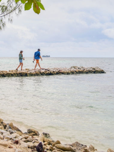 A couple walking out onto a stone outcrop into a tropical sea.