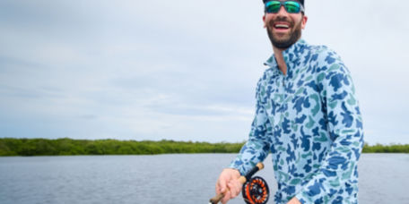 An angler in blue camo smiles while fly fishing.