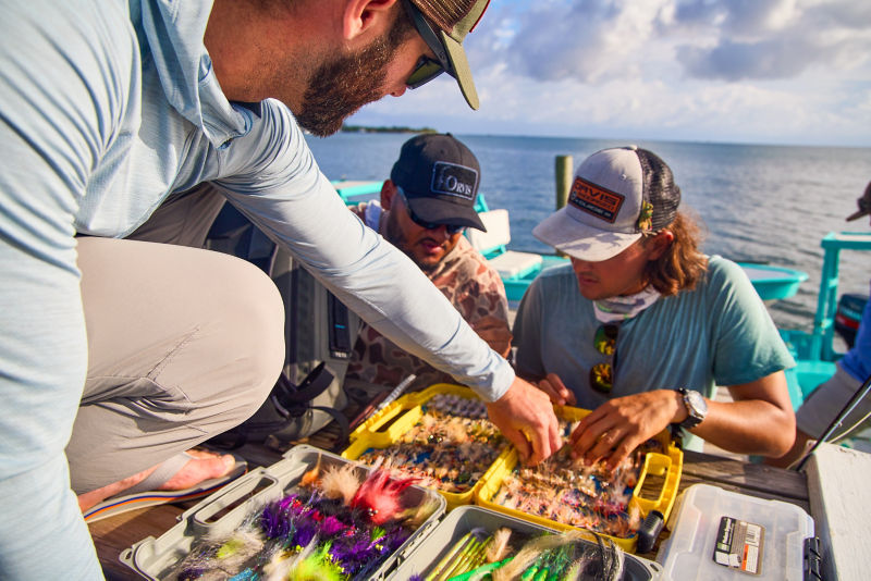 Anlgers pick flies from their fly box on a skiff.