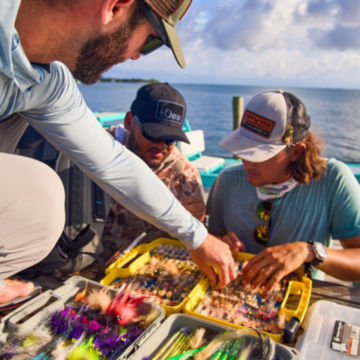 Anlgers pick flies from their fly box on a skiff.