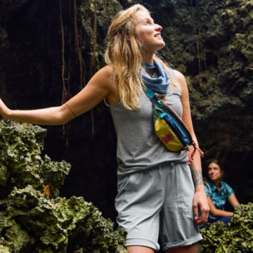 Woman looks up from rock cavern while on a hike.