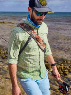 An angler walks along a rocky beach.