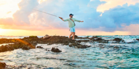 An angler standing on rocks oceanside mid cast.