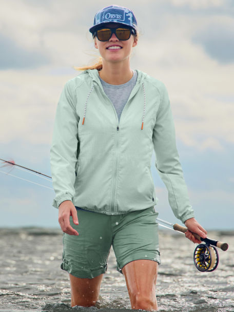 Woman wading with rod wearing light green open air casting jacket