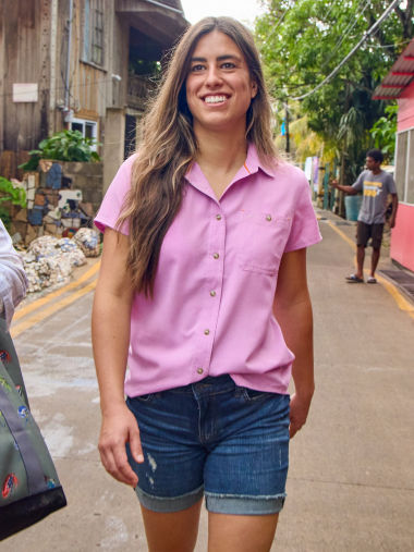 A woman walking on a street wearing a pink shirt and jean shorts.
