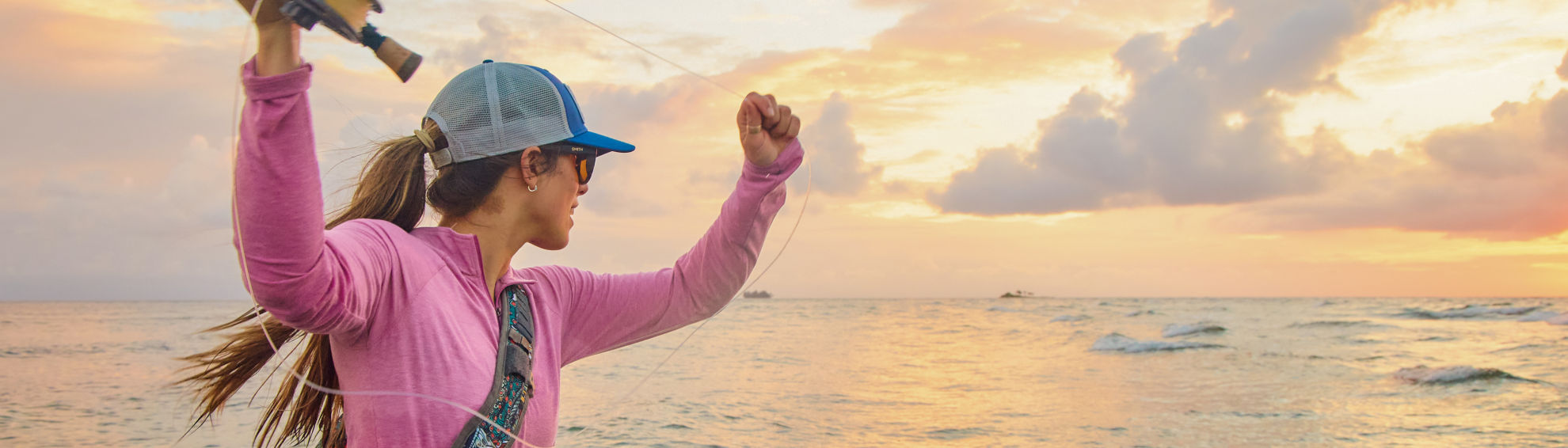 An angler casts her rod as the sun rises over the ocean.