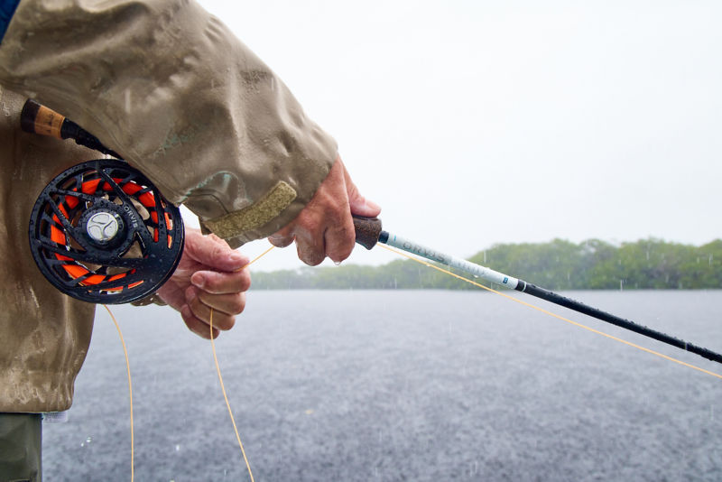 An angler holds his rod with a Mirage reel as he casts into the rain.