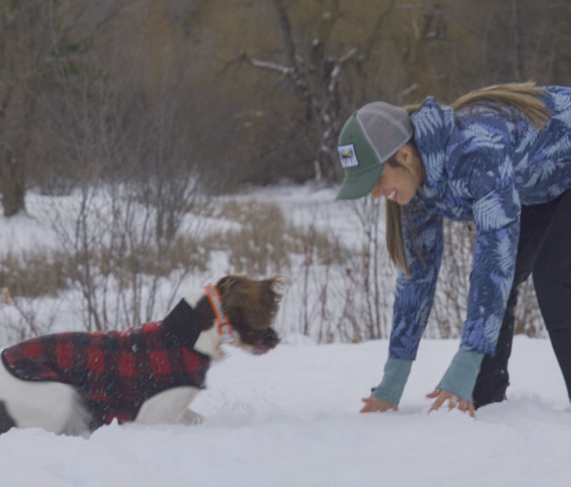 A woman bending down playing with her dog in a warm winter coat