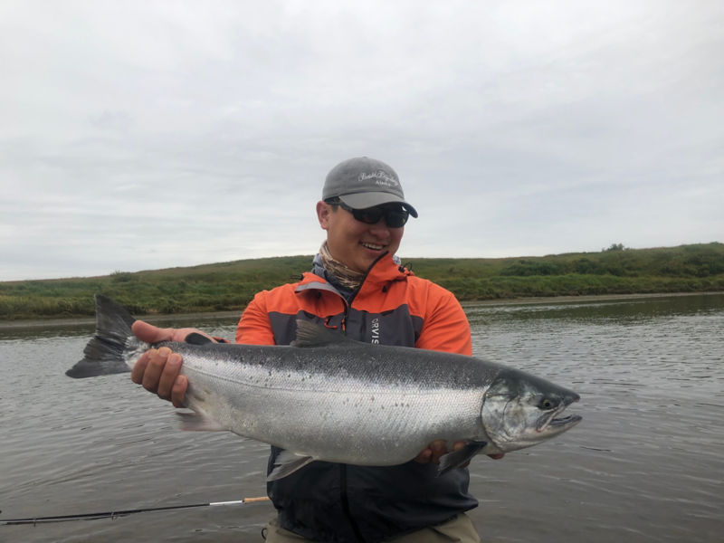 Ian Huang holding a giant silver fish under a cloudy sky.