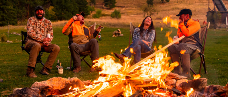A group of people sit around a blazing bonfire laughing together