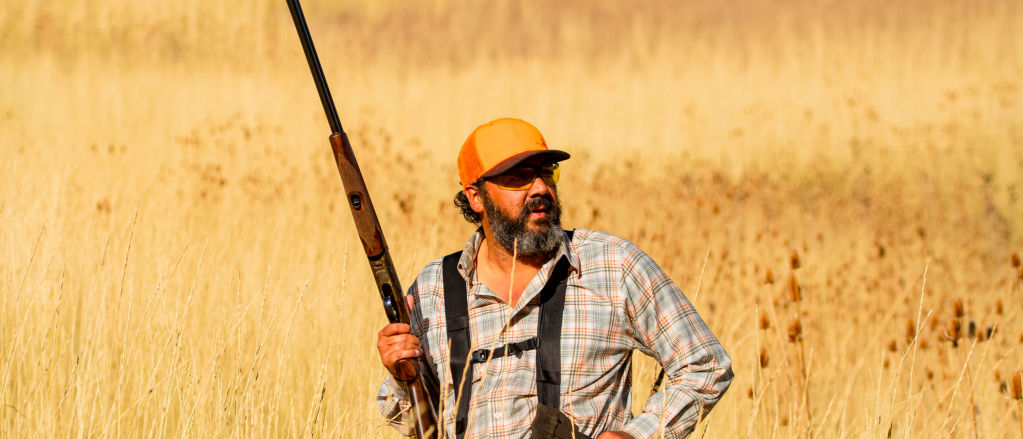 A hunter carrying a shotgun through an upland field