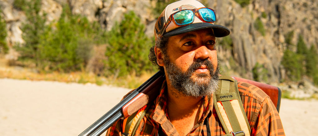 A hunter in cap and sunglasses holding a shotgun