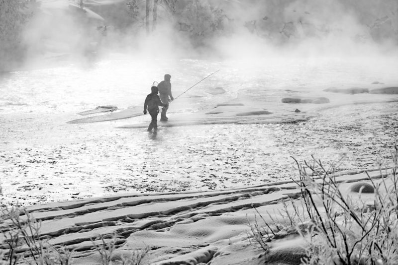 Black and white image of two people walking through a lake.