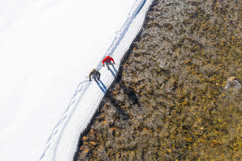 A shot from above of two anglers walking in the snow alongside an icy river