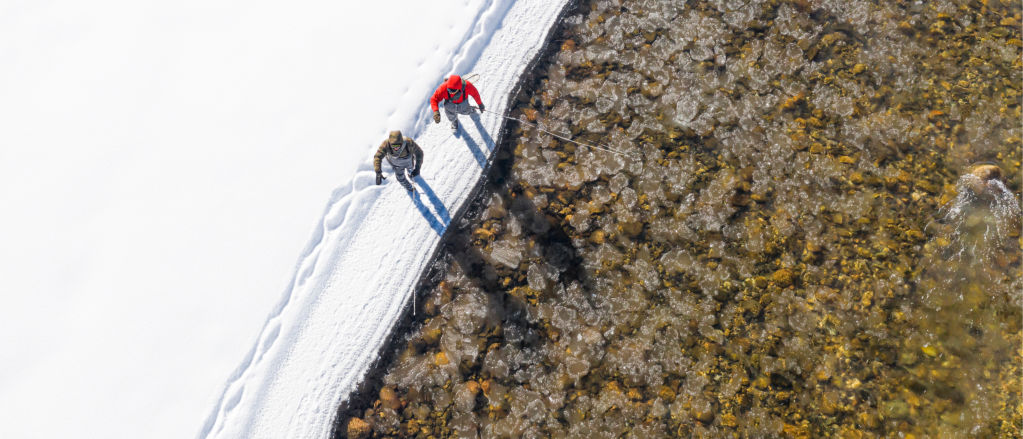 A shot from above of two anglers walking in the snow alongside an icy river