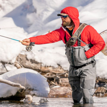 An angler casts his rod in a frozen river.