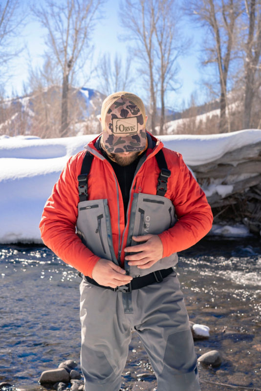 An angler wearing a red jacket adjusts the zip of their waders