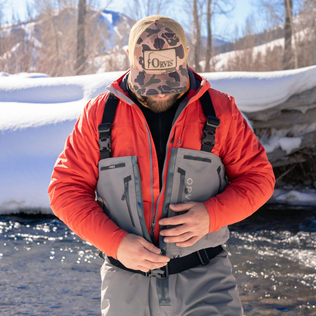 An angler wearing a red jacket adjusts the zip of their waders