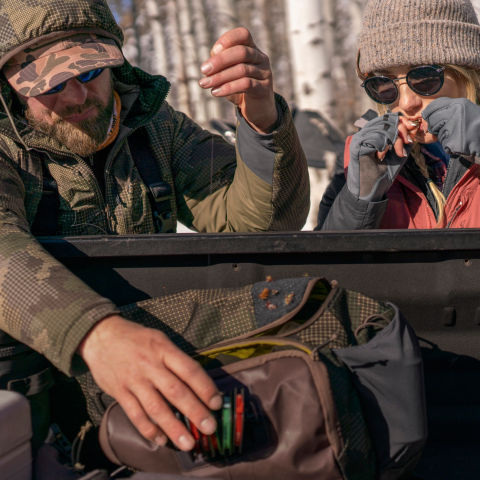 Two anglers gear up at the back of a truck in a snowy wood