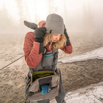 An angler bundles up in cold-weather gear before she wades into an icy river.