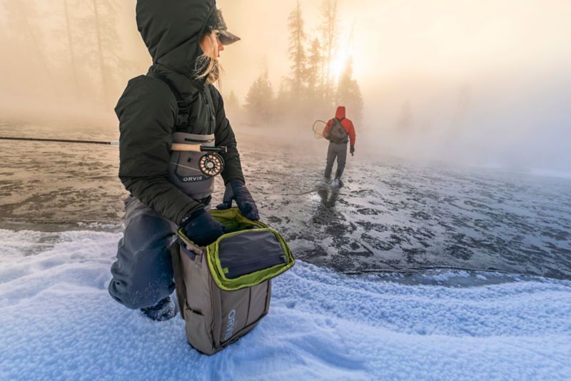 The sun rises on an icy foggy morning with two anglers in full insulated gear.